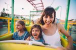 Excited little boy and girl having fun with mother riding amusement park roller coaster