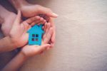 Adult and child hands holding paper house, keeping the family home concept